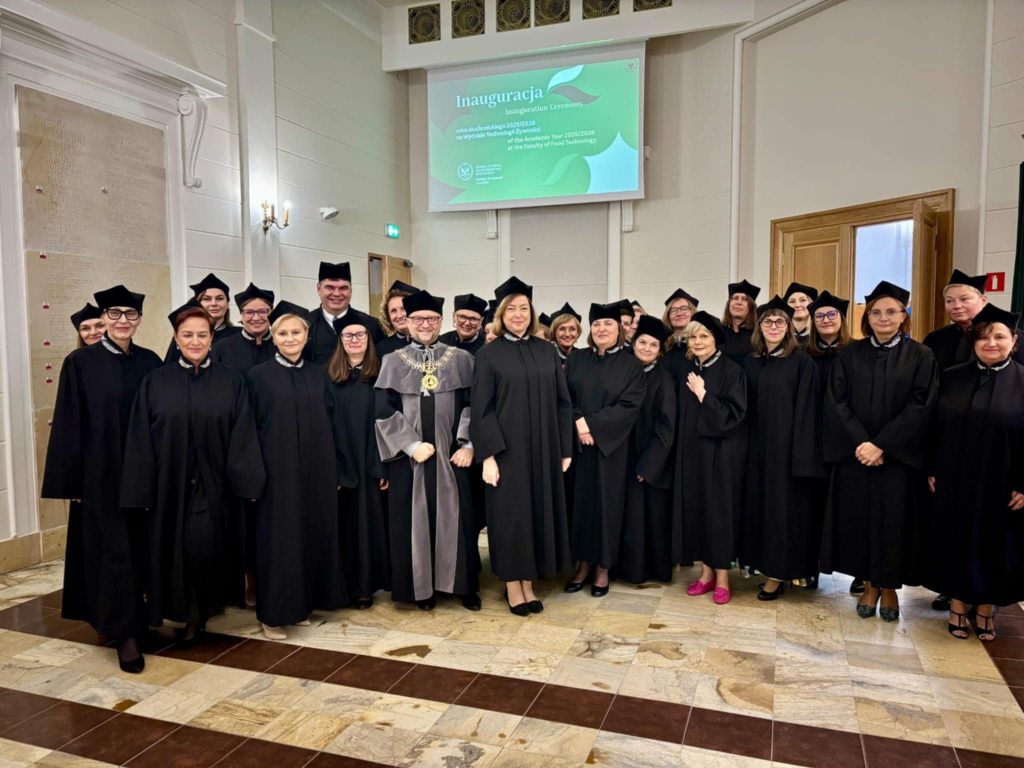 Grupa nauczycieli akademickich w togach stoi przed aulą